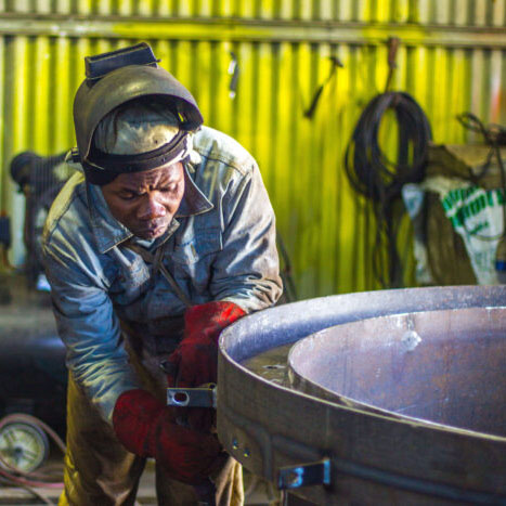 floor operator inspecting large tank machine with welding mask