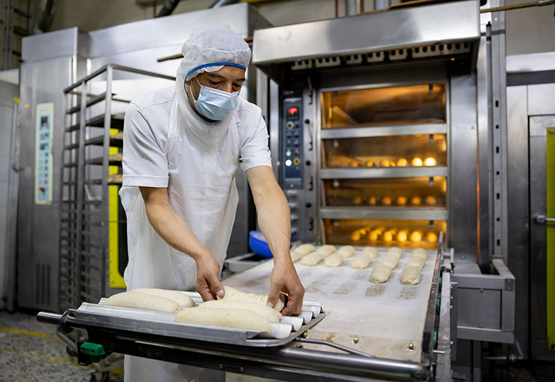 Latin American worker baking bread at an industrial bakery -manufacturing concepts