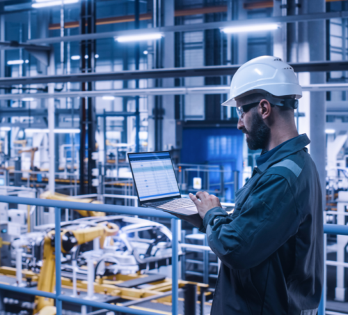 employee holding laptop overseeing shop floor from above