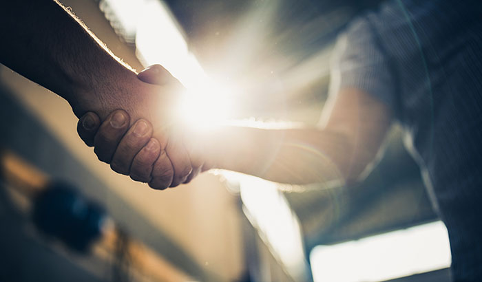 Close up of unrecognizable men handshaking in a factory.