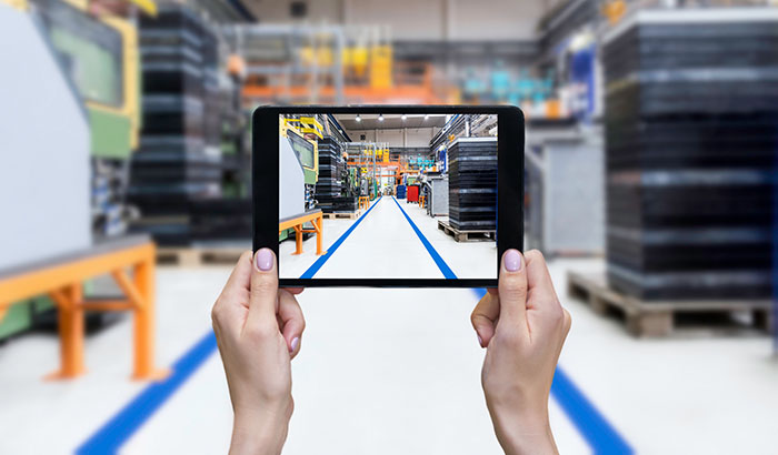 Horizontal color image of female hands holding a digital tablet in a modern plastic production line. Ordering on-line from injection moulding factory on a touchscreen tablet computer. Industrial aisle surrounded by modern equipment and machines which having busy robotic arms with molding shapes and producing plastic pieces for variety of industry. Labor intensive production line with manufacturing equipment - boxes, crates, packages, pallets,... Manufacturing equipment arranged on clean and shiny flooring in background.