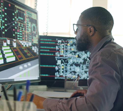 tock image of an Afro-Caribbean male designing electronic circuit boards ( PCBs). He’s sitting at a desk with a large computer screen displaying a variety of apps