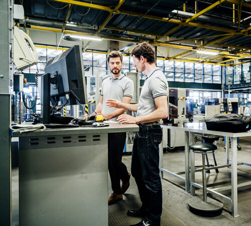 Two printing factory engineers working at a console together.