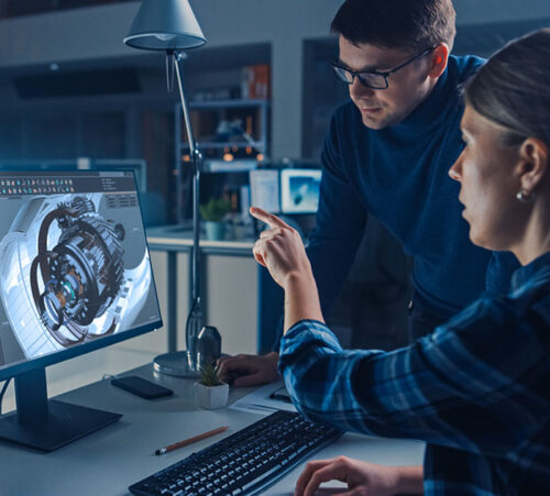 Engineer Working on Desktop Computer, Screen Showing CAD Software with Engine 3D Model, Her Male Project Manager Explains Job Specifics. Industrial Design Engineering Facility Office