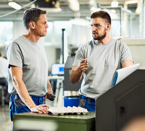 Two male coworkers communicating while working in industrial building.