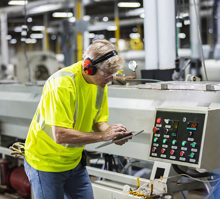 Senior man in factory at control panel, digital tablet