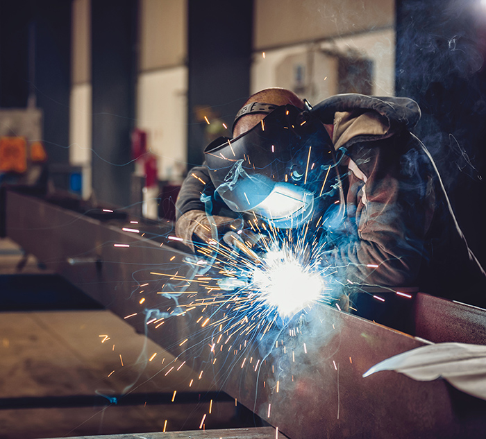 Industrial Welder With Torch and Protective Helmet in big hall welding metal profiles