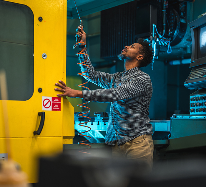 Adult Black Electrical Engineer Preparing To Clean The CNC Machine With An Air Blow Gun In A Factory