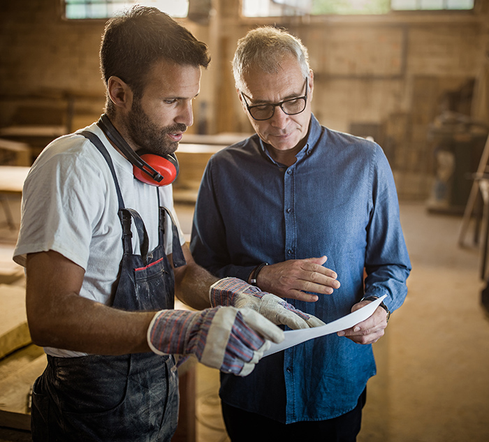 Mature manager and carpenter analyzing design plans in a workshop.