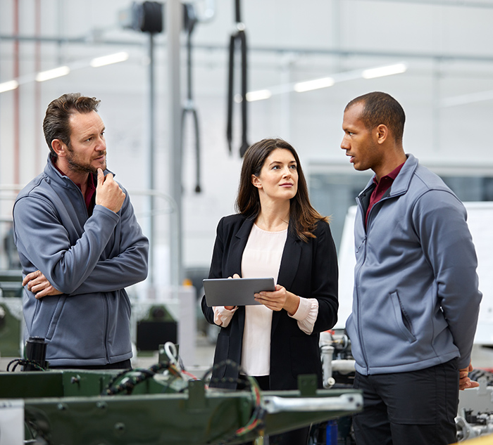 Automobile engineer discussing with colleagues in car factory. Multi-ethnic male and female professionals are standing at car production line. They are in automotive industry.