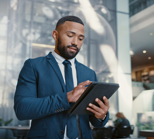 Hotel, manager and man on a digital tablet for booking, planning and accommodation management while working at front desk. Black man, concierge and hospitality by male doing online task at reception