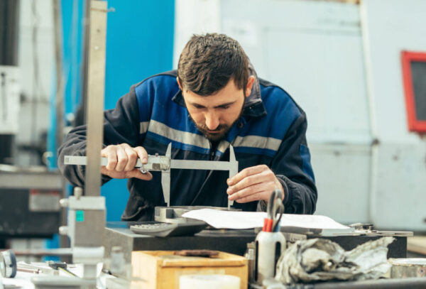 Worker measuring metal part in factory