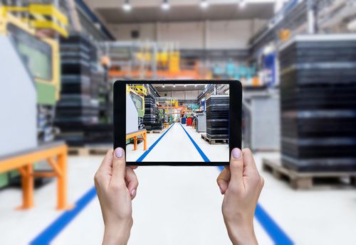 female hands holding tablet looking onto manufacturing shop floor
