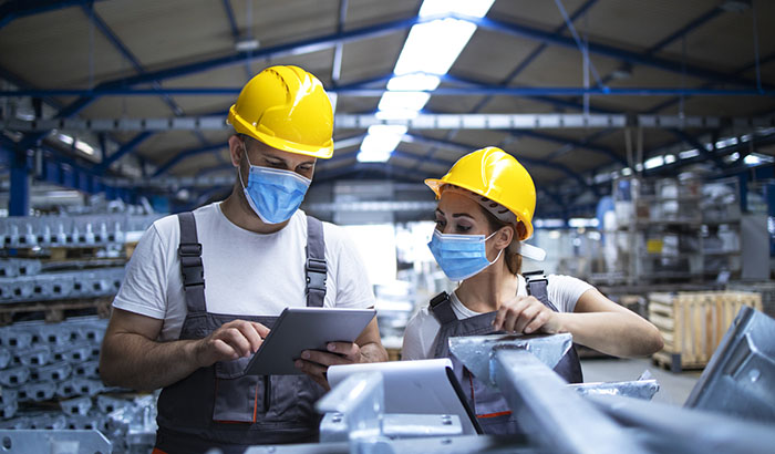 Industrial workers with face masks protected against corona virus discussing about production in factory. People working during COVID-19 pandemic.